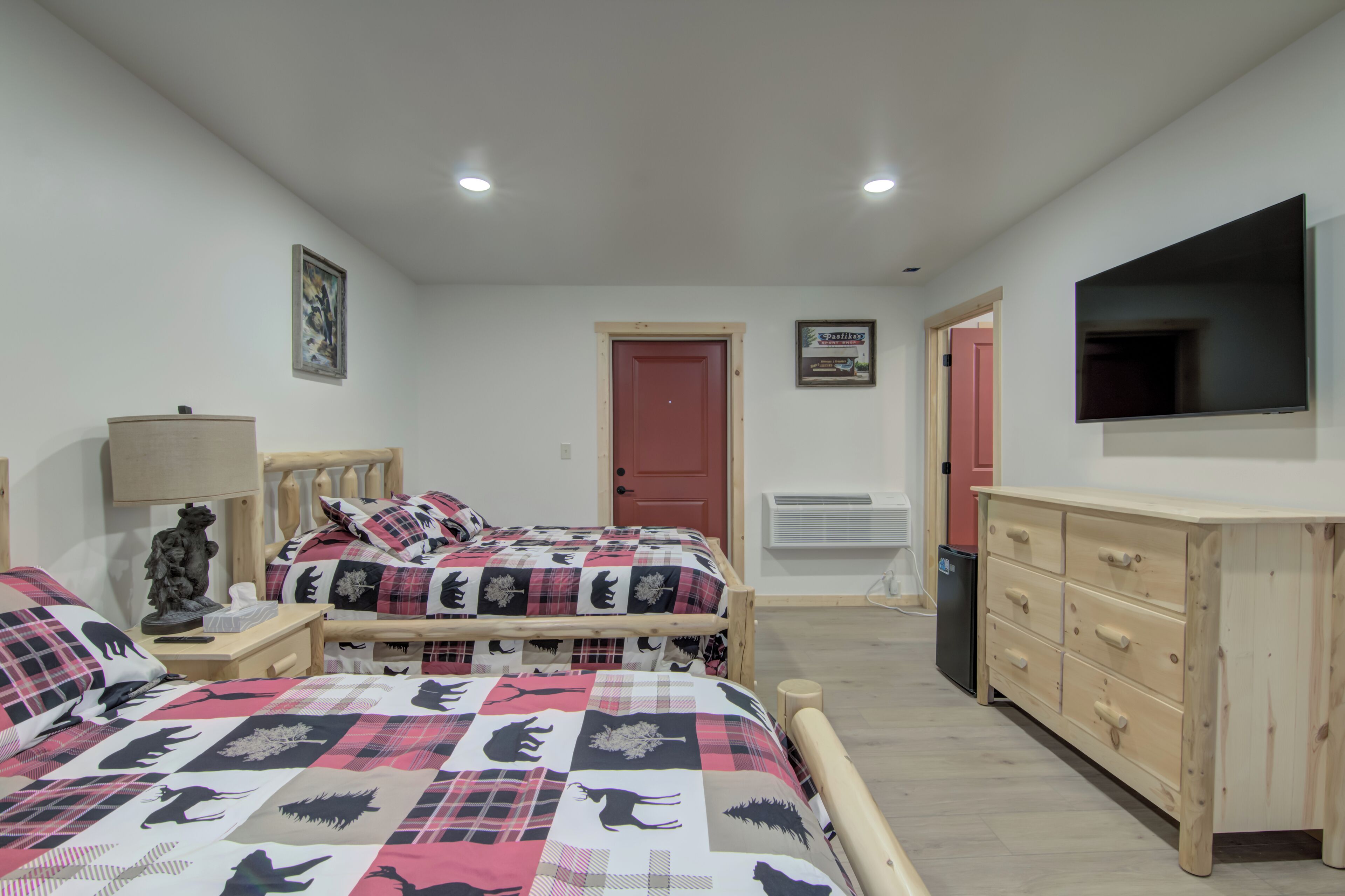 Een slaapkamer met twee bedden, een kapstok, een televisie en een deur.
