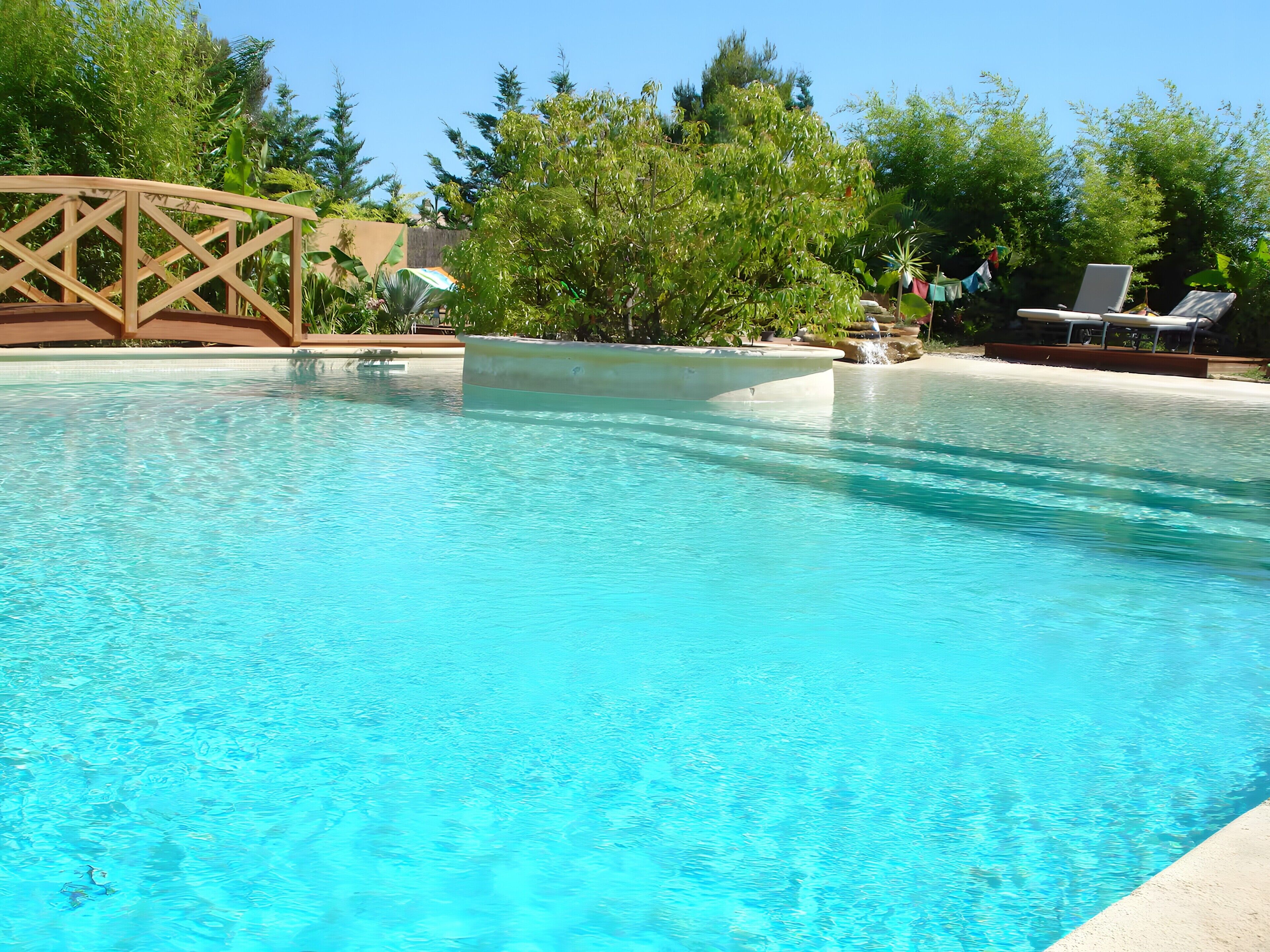 Une piscine aux eaux cristallines, dotée d’une terrasse en bois et de chaises longues.
