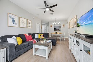 Ein modernes Wohnzimmer mit einem grauen Sofa, einem weißen Couchtisch und einem Fernseher auf einer Holzkommode.