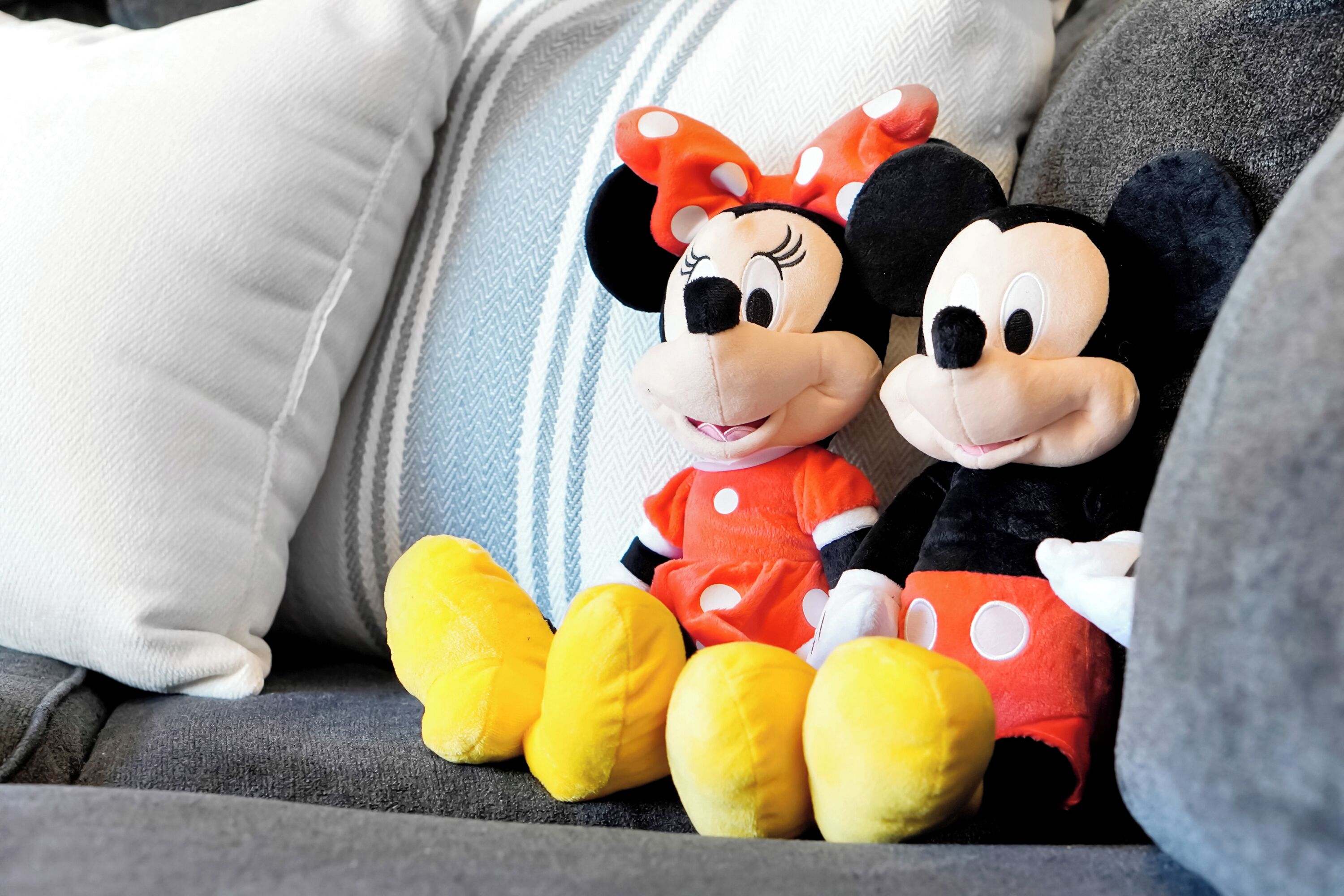 Two plush toys on a grey sofa with a patterned cushion.