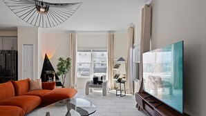 Ein modernes Wohnzimmer mit einem Ecksofa, einem Glastisch, einem großen Flachbildfernseher und einer außergewöhnlichen Deckenleuchte.
