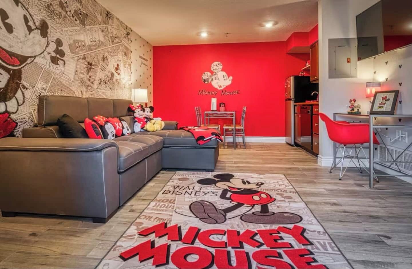 A Mickey Mouse-themed living room with a red wall, a grey sofa, and a Mickey Mouse rug.