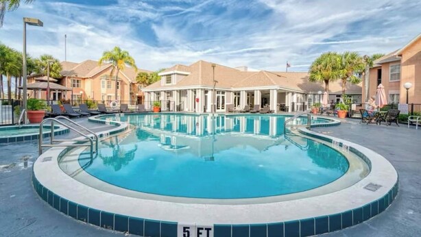 Une piscine dont la profondeur est indiquée à 1,5 mètre, entourée de chaises longues et de parasols, avec des bâtiments en arrière-plan.