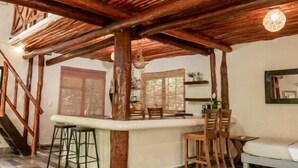 A spacious room with a high ceiling supported by wooden beams, a glass table, and a bar area with stools. - La Casa de Mia Tulum (Tulum)
