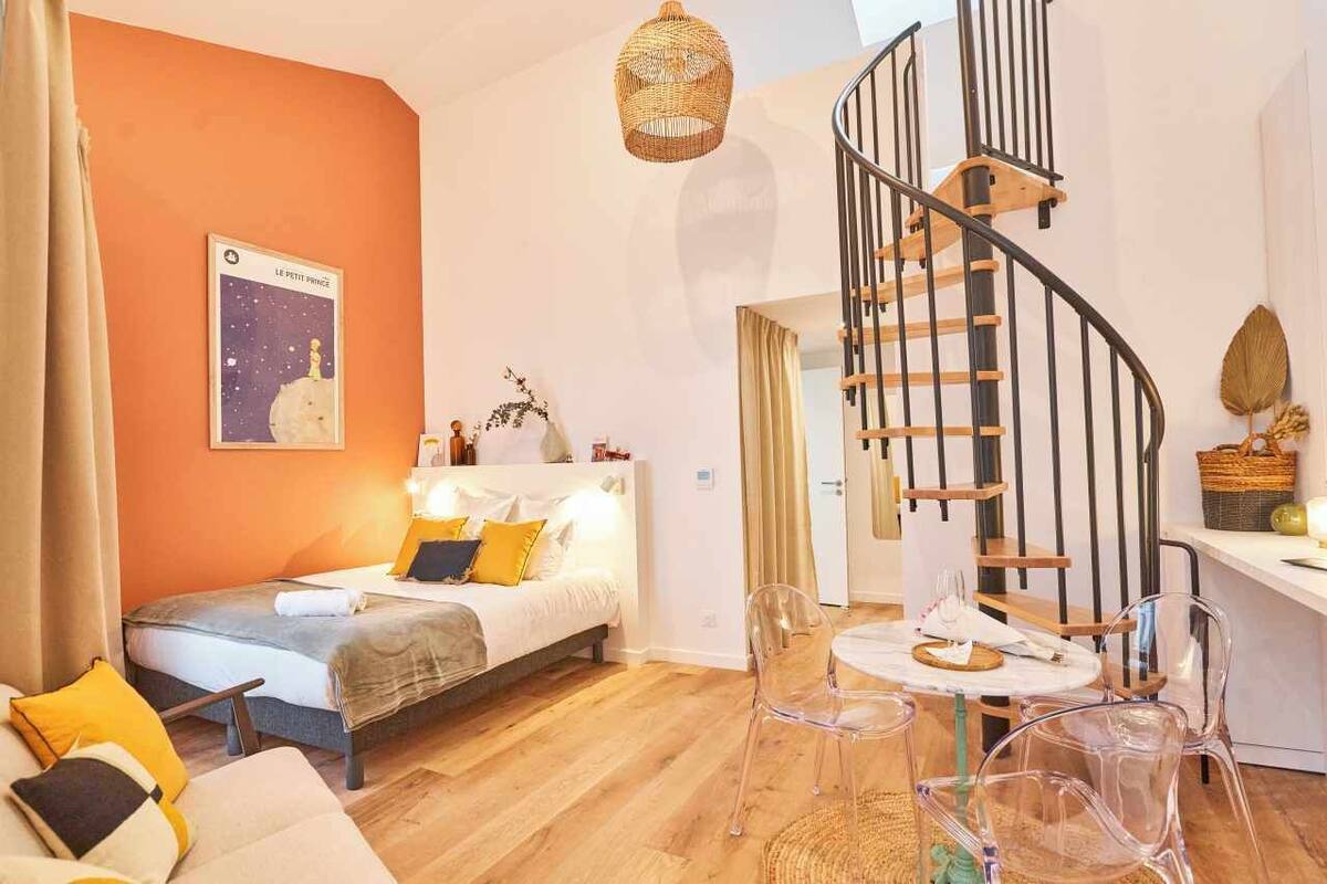 Ein gemütliches Zimmer mit einem Bett, einem Esstisch mit Stühlen, einer Treppe und einer Wand mit einem Poster.