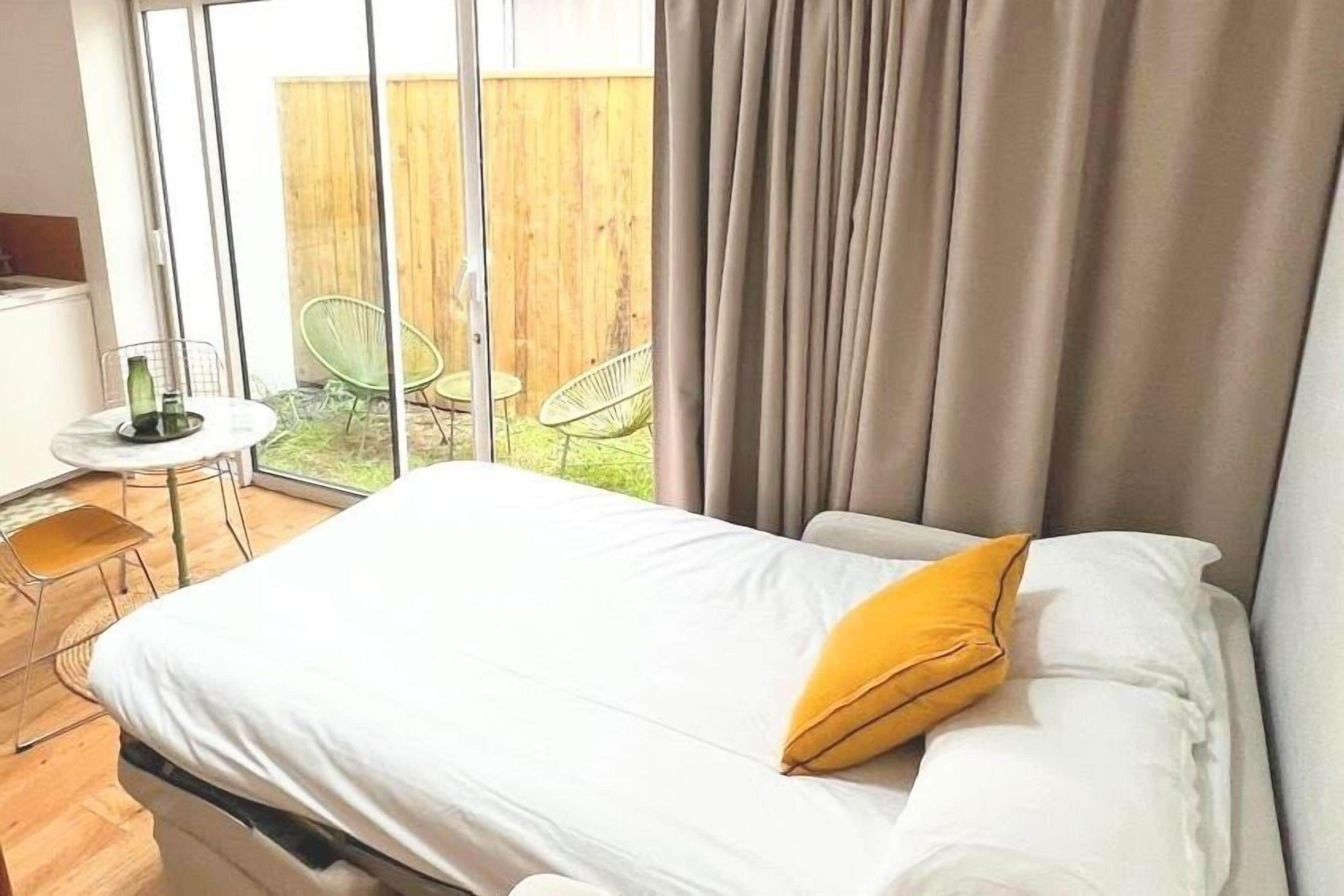 Une chambre à coucher avec un lit, une fenêtre et une vue sur un espace extérieur aménagé avec des chaises et une table.