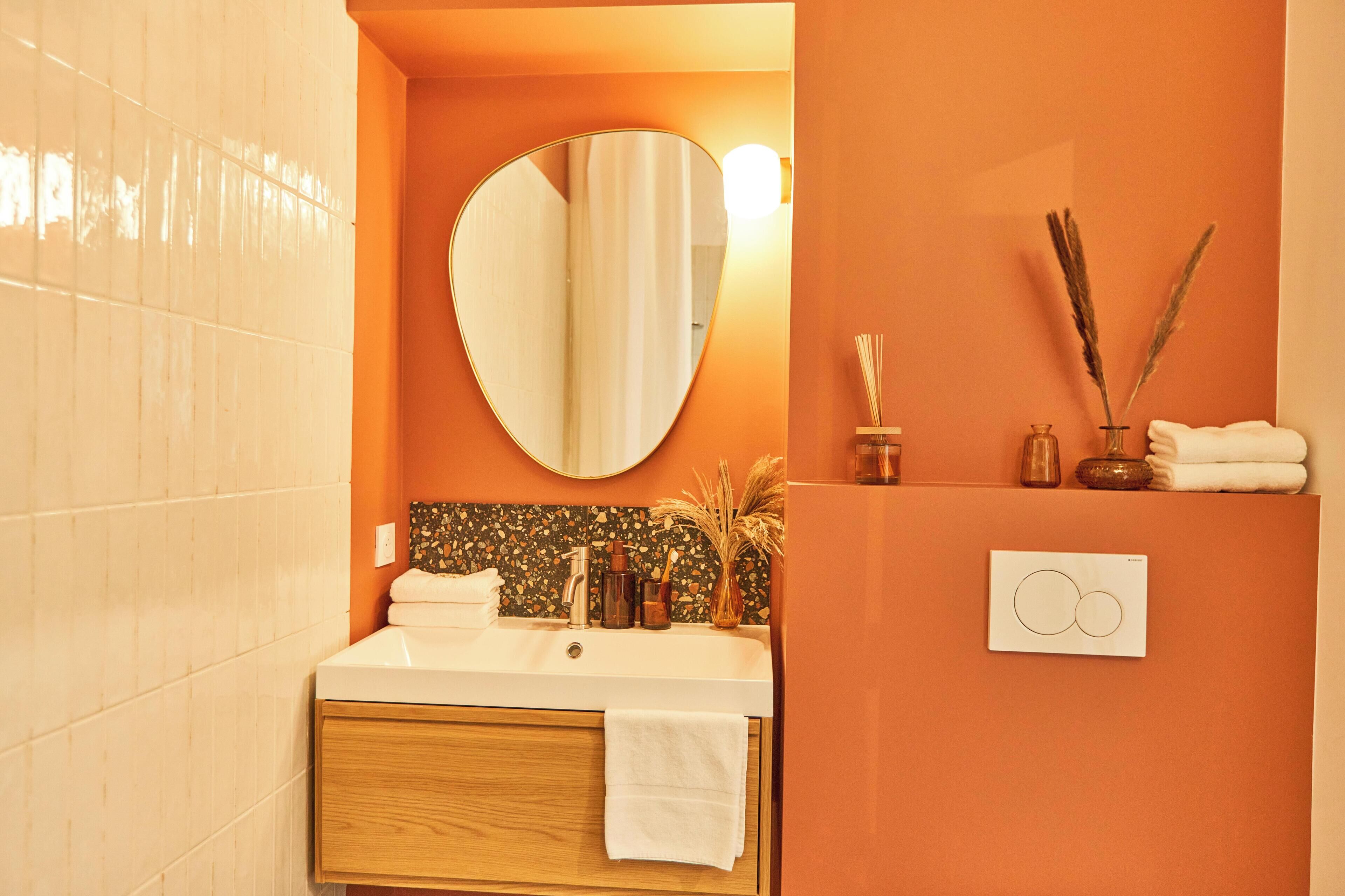 A bathroom with a white sink, a mirror, and a wall-mounted light. There are towels and a vase with decorative reeds on the counter.