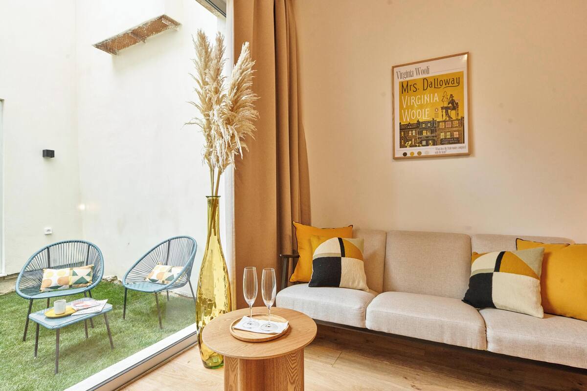 Ein Wohnzimmer mit einer Couch, zwei Sesseln, einem runden Holztisch mit Gläsern, einer Vase mit Pampasgras und einem Poster an der Wand.