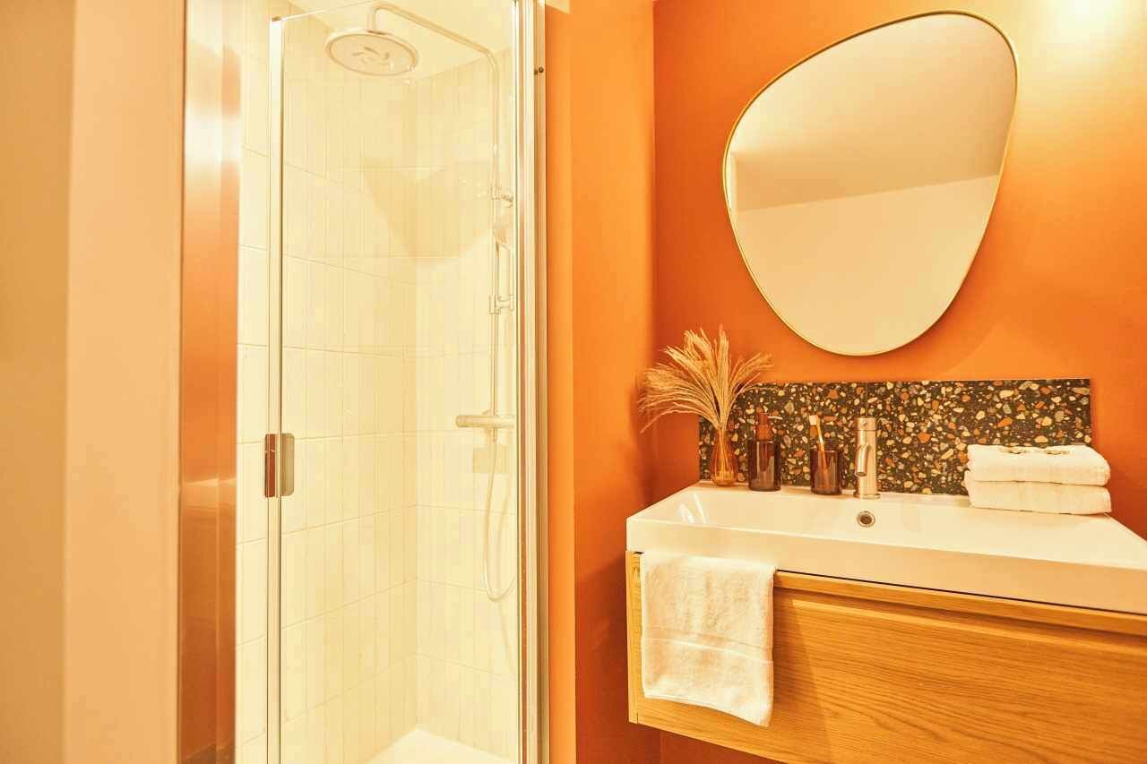 Un baño con cabina de ducha de vidrio, un lavamanos blanco con mueble de madera y un espejo decorativo en la pared.