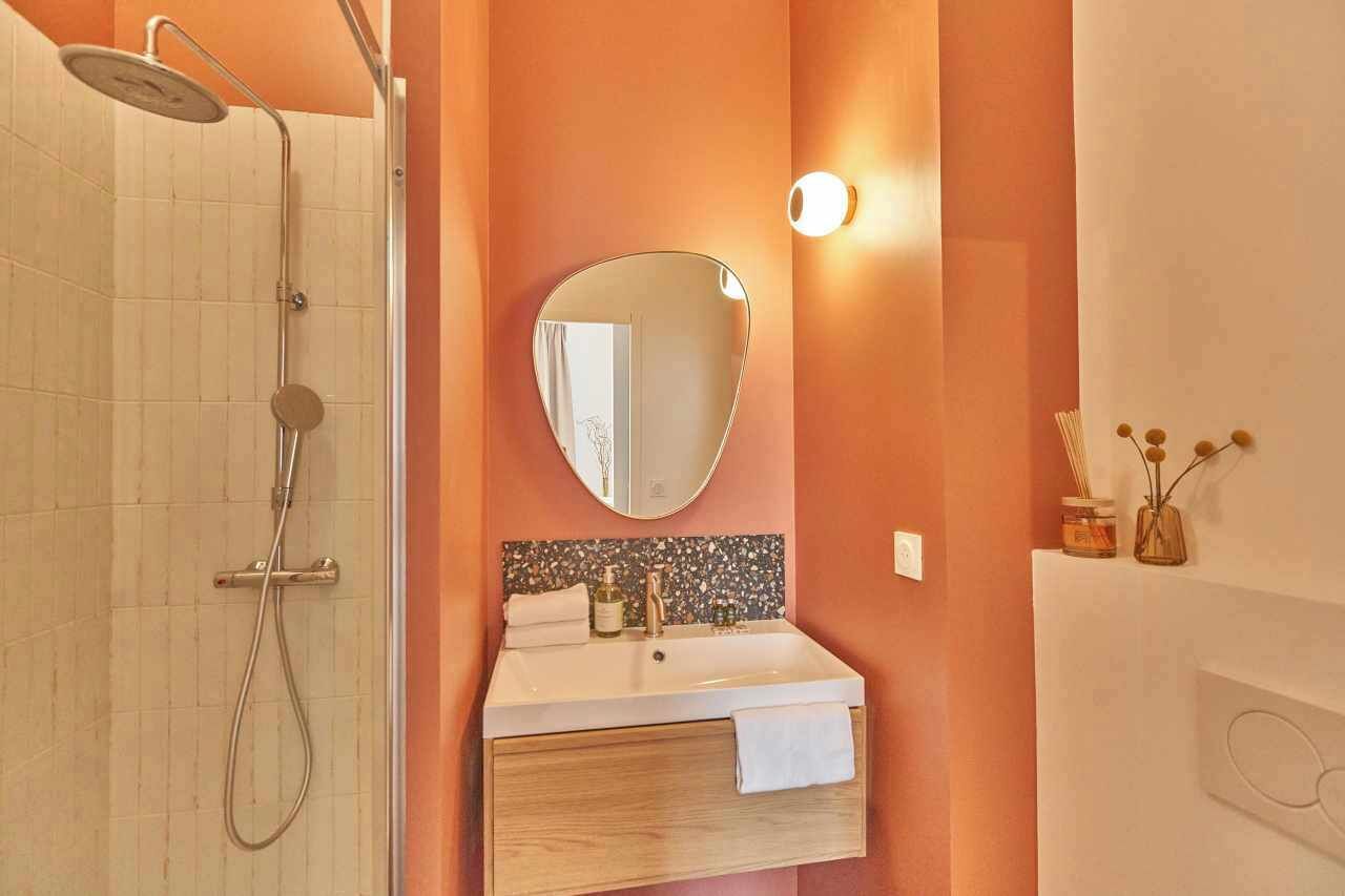 Ein Badezimmer mit Dusche, Waschbecken inklusive Spiegel und einer Wandleuchte.