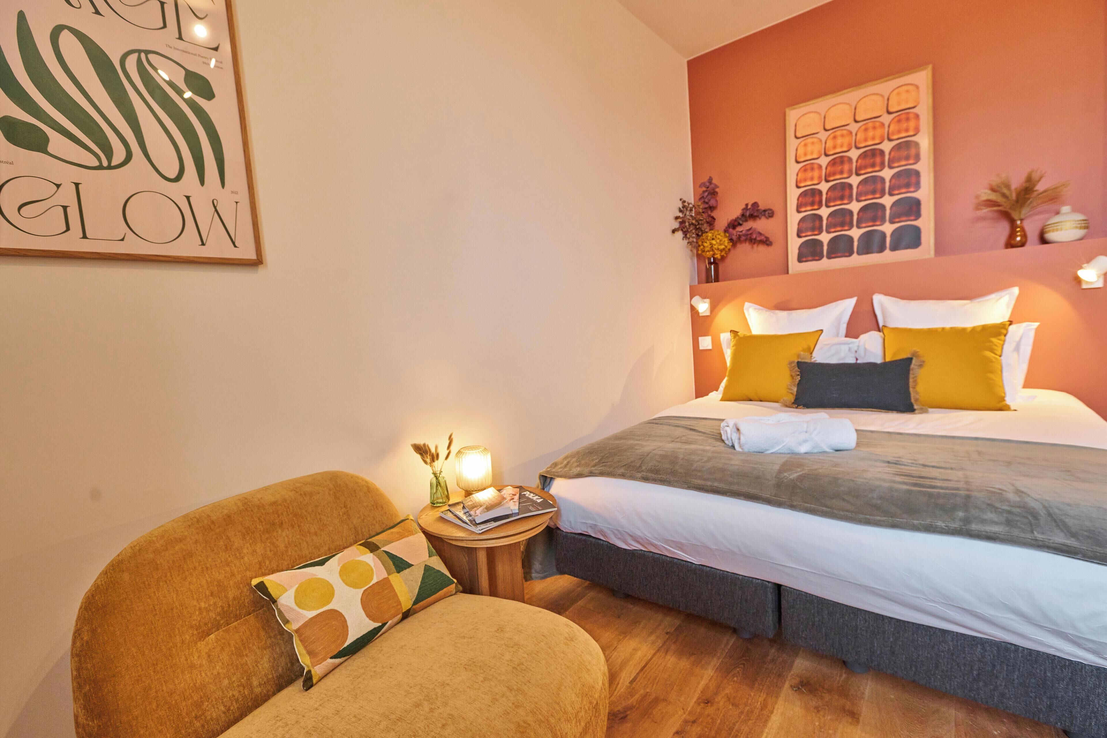 Un dormitorio con una cama, una silla, una mesita de noche y un cuadro en la pared.