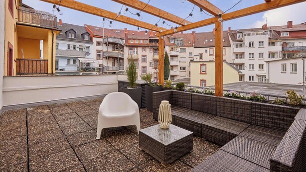 A rooftop terrace with a wooden pergola, outdoor seating, and a view of surrounding buildings. - Bella - Kaiserslautern (Kaiserslautern)