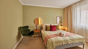 A bedroom with a bed, a chair, a bedside table, a mirror, and a window with curtains. - Bella - Kaiserslautern (Kaiserslautern)