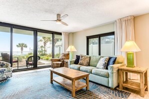 A spacious living room with a large window, a ceiling fan, a sofa, a coffee table, and two lamps. - Watercrest 110 (Panama City Beach)