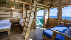 A wooden cabin with bunk beds, a ladder, and a view of the ocean.