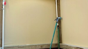 A corner of a room with a wooden ceiling and a green hose attached to a wall-mounted valve.