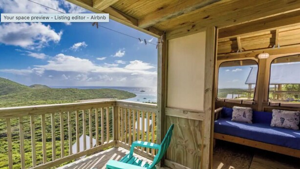 A wooden deck with a view of a coastal landscape, a blue sofa, and two turquoise chairs.