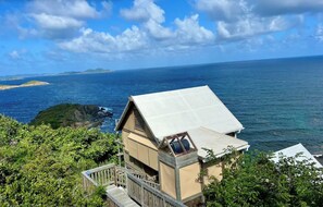 A coastal property with a wooden deck and a large window overlooking the sea. - Eco Cabin in Paradise (St John)