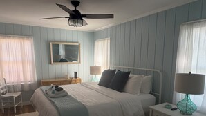 Quarto bem organizado com cama, mesas de cabeceira, espelho e ventilador de teto.