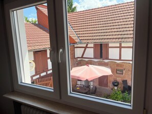 A window with a view of a courtyard featuring a brick building, a wooden fence, and a table with an umbrella. - Villa Filimena Monteurunterkunft Gründau (Gruendau)
