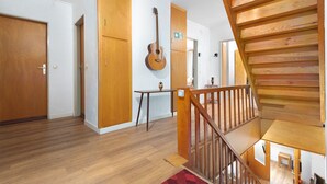 Una habitación con suelo de madera, una escalera y una guitarra en la pared.