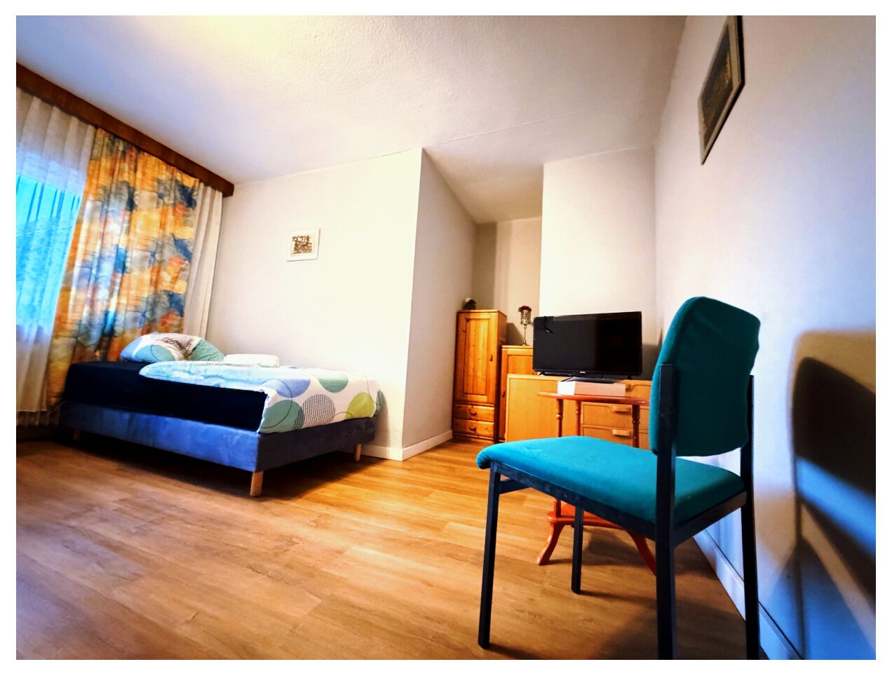 A bedroom with a bed, a desk with a television, a chair, and a wardrobe.