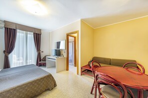 A hotel room with a bed, a desk, a computer, a sofa, and a dining table with chairs. - Charming Rina Sea Studio Apartment-central Air-con & Wifi Sleeps 2 Persons (Alghero)