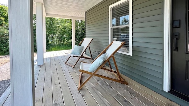 A covered porch with two wooden lounge chairs and a window. - Lake Street Retreat - Walk to the beach! (Central Lake)