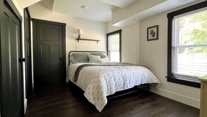 A bedroom with a bed, a window, a door, and a wall-mounted shelf. - Lake Street Retreat - Walk to the beach! (Central Lake)