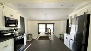 A modern kitchen with a central island, stainless steel appliances, and white cabinetry. - Lake Street Retreat - Walk to the beach! (Central Lake)