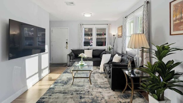 Een moderne woonkamer met een flatscreen televisie, een zwarte bank, een glazen salontafel en een vloerkleed met dessin.