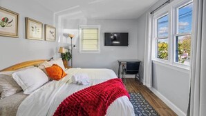 Een slaapkamer met een bed, bureau, televisie en grote ramen.