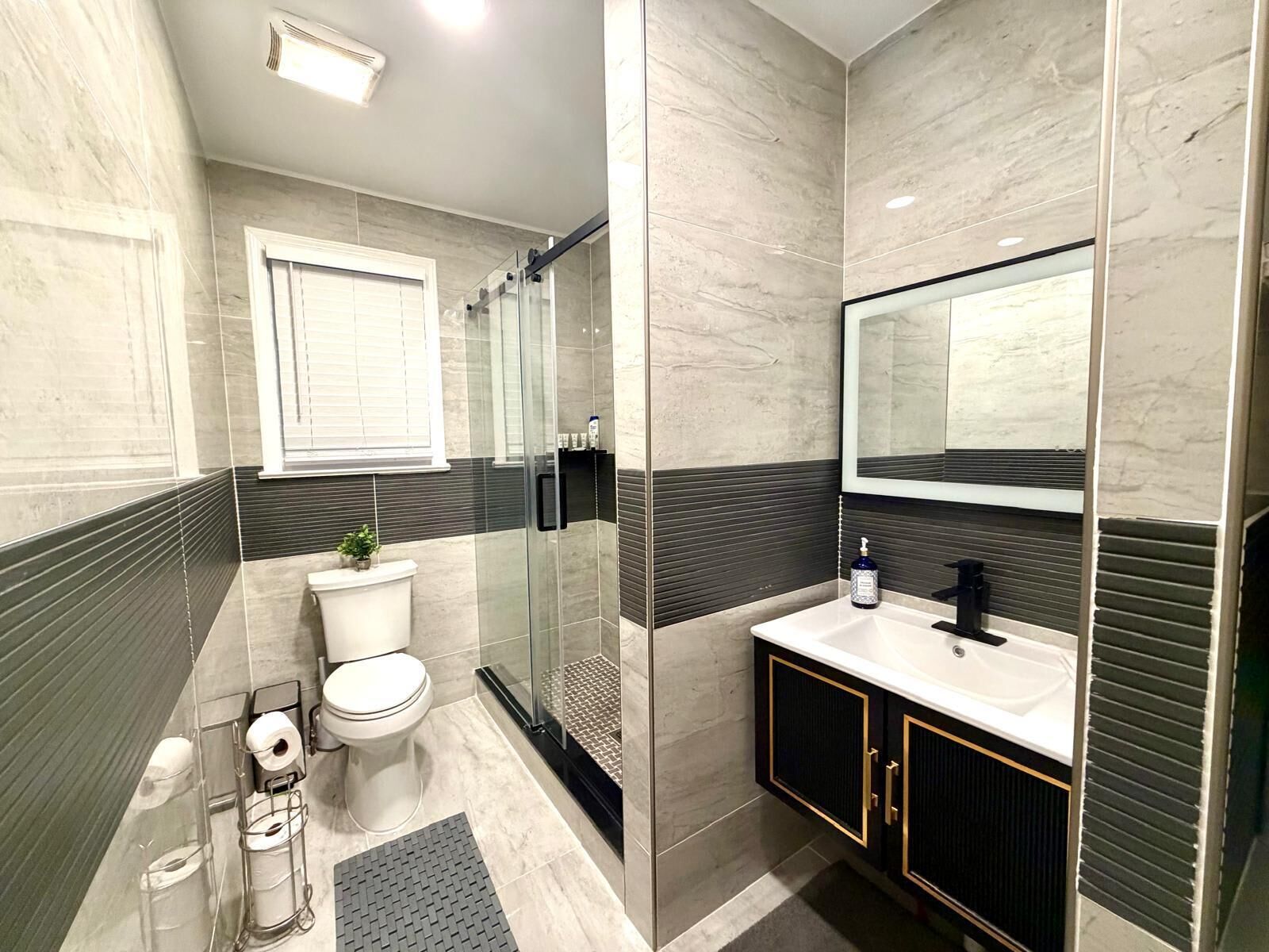 A modern bathroom with a toilet, sink, and shower area, featuring a large mirror and a potted plant.