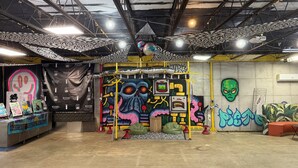 Et rum indendørs med en væg dækket af graffiti, en trækonstruktion og et bord med genstande på.