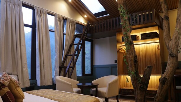 A bedroom with a bed, two chairs, a small table, a ladder, and a large window with curtains. - SnugBug Kasol (Kasol)