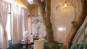 A room with a dining table, chairs, a vase with flowers, and a large tree trunk. - SnugBug Kasol (Kasol)