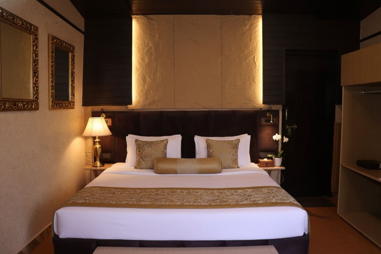 Ein Hotelzimmer mit einem großen Bett, einem Nachttisch mit Lampe und einem an der Wand befestigten Spiegel.