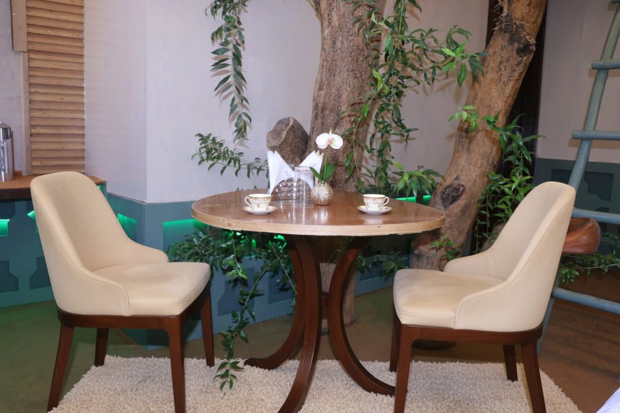 A round wooden table with two beige chairs, a vase with an orchid, and two cups.
