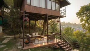 A wooden cabin with a balcony, outdoor seating, and a fire pit. - SnugBug Kasol (Kasol)