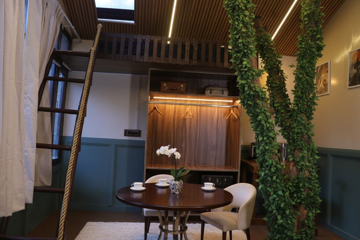 A dining area with a round table, chairs, a vase with flowers, and a wooden cabinet in the background.