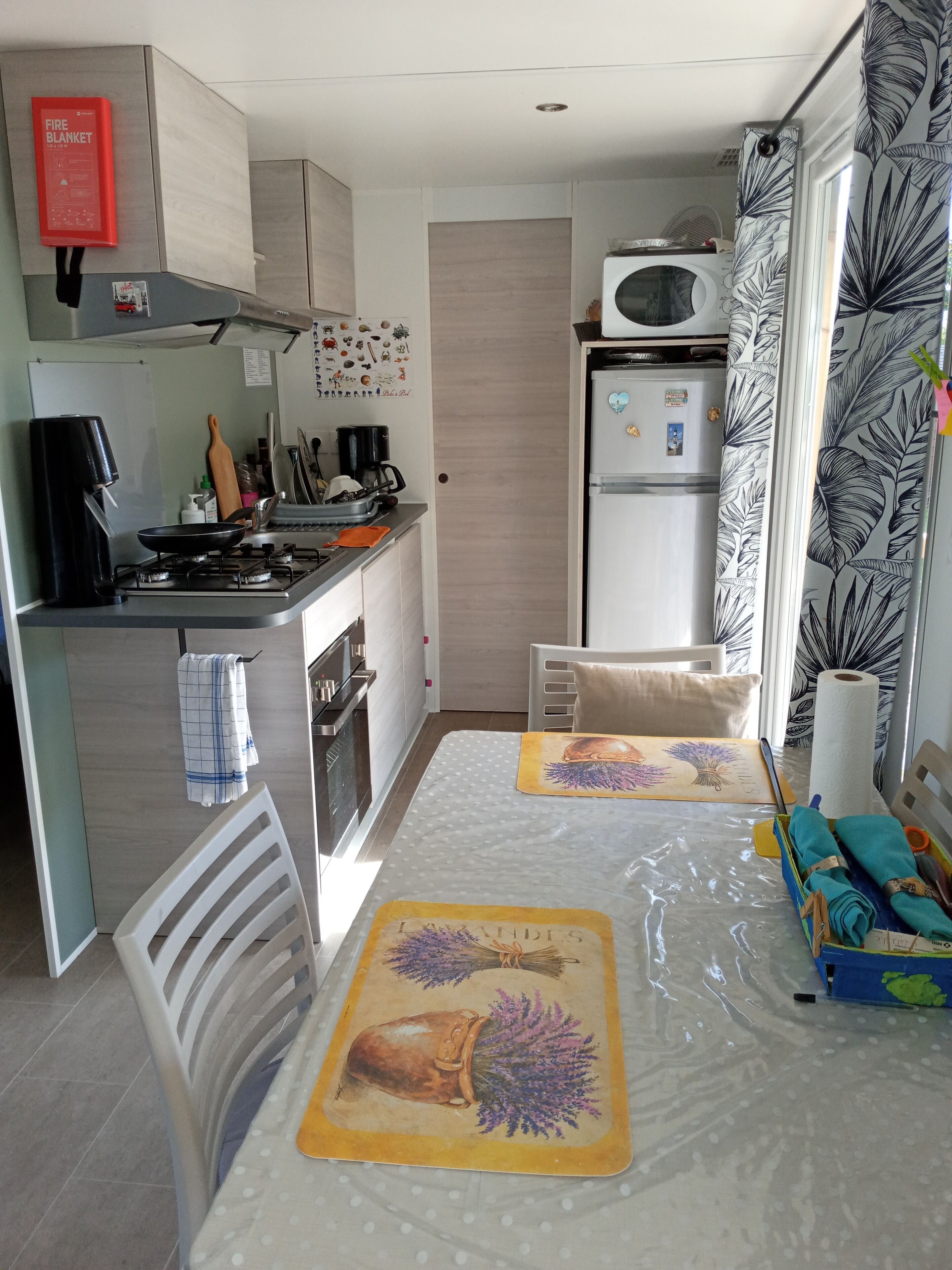 A compact kitchen with a gas stove, microwave, and a refrigerator. There is a dining table with placemats and a chair.
