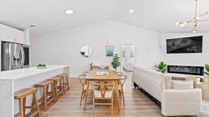 A modern kitchen with white cabinetry, a wooden dining table, and bar stools. - Sandpiper Sanctuary – Beach Retreat, Sleeps 14 (Myrtle Beach)