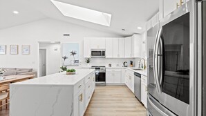 A modern kitchen with white cabinetry, a large island, stainless steel appliances, and a skylight. - Sandpiper Sanctuary – Beach Retreat, Sleeps 14 (Myrtle Beach)