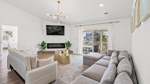 A modern living room with a sectional sofa, a flat-screen TV, and a unique chandelier. - Sandpiper Sanctuary – Beach Retreat, Sleeps 14 (Myrtle Beach)
