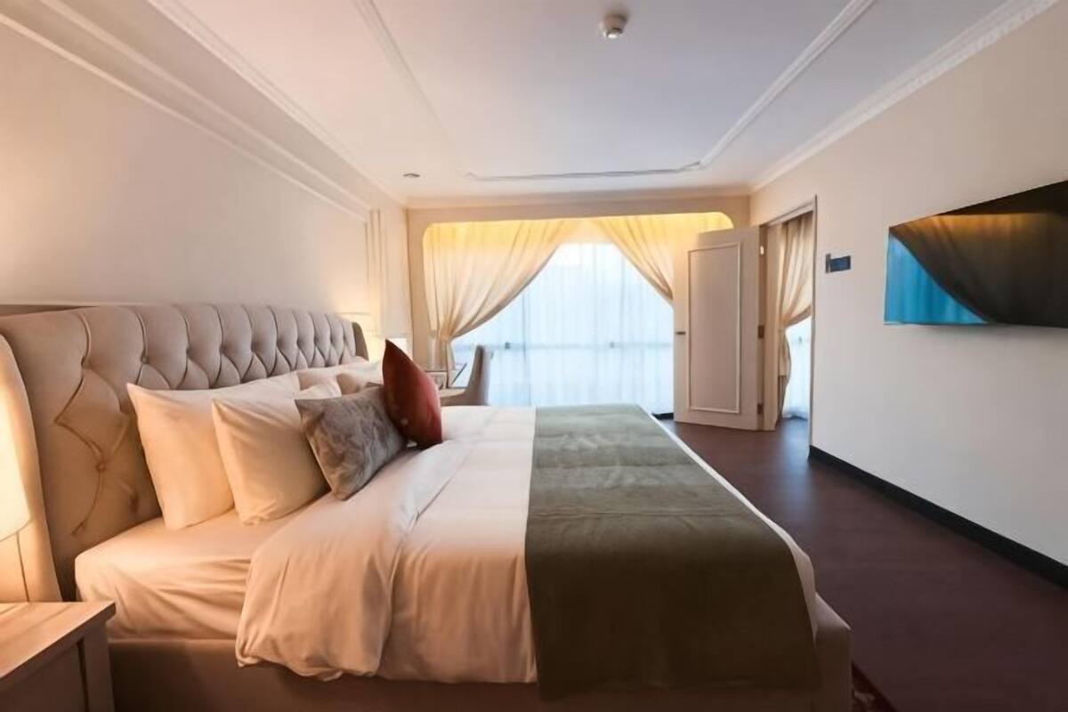 Een hotelkamer met een groot bed, een nachtkastje, een raam met gordijnen en een schilderij aan de muur.