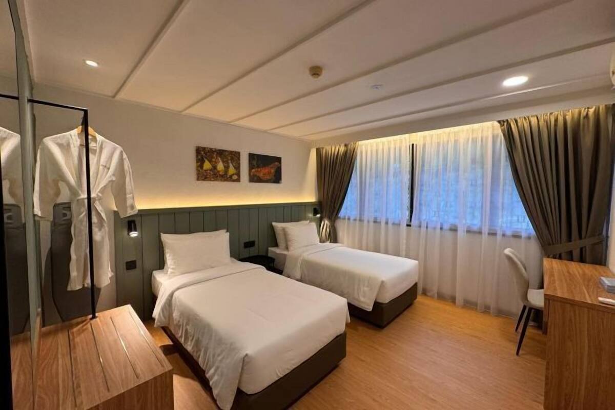 Een hotelkamer met twee bedden, een bureau, een stoel, een spiegel en een raam met gordijnen.