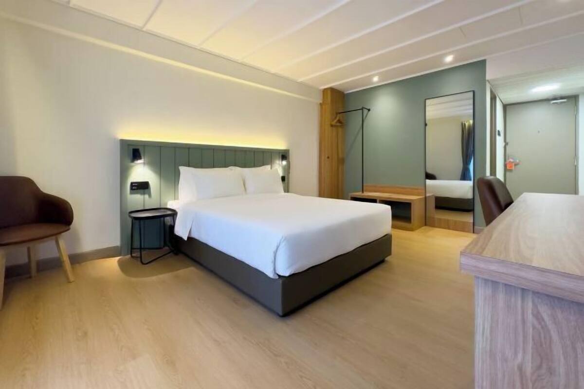 Een moderne hotelkamer met een bed, nachtkastje, stoel en bureau met spiegel.