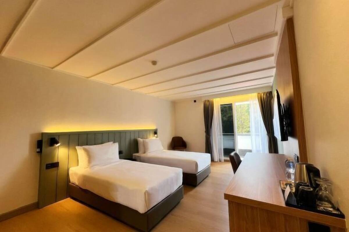 Een hotelkamer met twee bedden, een bureau en een raam met gordijnen.