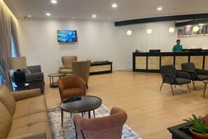 Un hall d’hôtel avec des canapés, des fauteuils, un comptoir d’accueil et un écran de télévision.