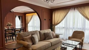 Un salon comprenant un canapé, un fauteuil, une table basse en verre et un coin repas avec une table et des chaises.